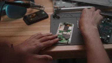 Tahta masadaki akıllı telefonu tamir ederken tornavida kullanan tanınmayan bir erkek öğrencinin omuz hizasında.