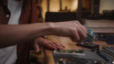 Gözlüklü delikanlının ahşap masada otururken akıllı telefonu tamir etmek için tornavida kullanışının yakın görüntüsü.