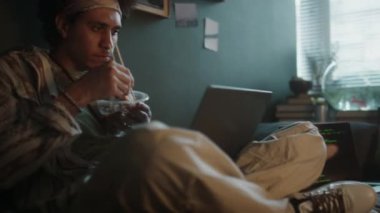 İki genç erkek müteahhit ellerinde kâse ve yemek çubuklarıyla dizüstü bilgisayar kullanırken