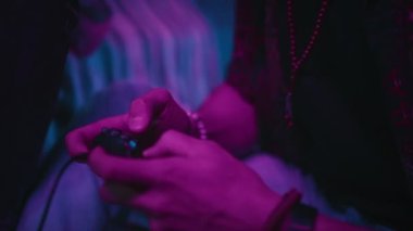 Yakın çekim, neon ışıklı odada arkadaşla oyun konsolu oynarken Z jenerasyonundaki adamın oyun sahasını gösterir.