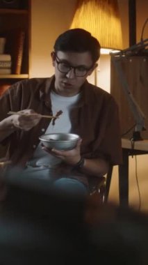 Gen Z programcısının yemek molasında evde bilinmeyen bir arkadaşıyla metal kaseden erişte yerken dikey görüntüsü.