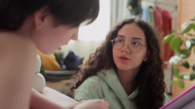 Çalışma kitabında ödevlerini tartışan iki genç kızın samimi yatak odasında ödevlerini yaparken yakın plan çekimleri.