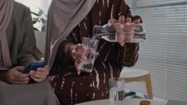 Müslüman bir kadının kızına bir bardak su dökerken ve dağıtırken, sonra da hastane lobisinde beklerken kitap okurken.