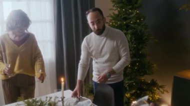 Bir çift birlikte yemek masası hazırlıyor ve evde Noel kutlaması için hazırlanırken arkadaşlarıyla cam parlatmakla ilgili konuşuyorlar.