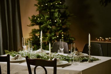 Boş parlayan tabaklar ve Noel partisi için dekore edilmiş yemek odasındaki sevimli çam çelenkli kristal bardaklarla dolu ahşap masa.