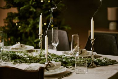 Orta boy söndürülmüş mumları gümüş şamdanlarla kaplayın. Masanın üzerinde çam çelenkleri ve şampanya için parlatılmış bardaklarla süsleyin.