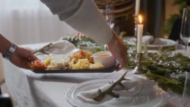 Erkeklerin ellerini kapat. Evde arkadaşlarıyla Noel yemeği hazırlarken yeşil çelenkler ve mum ışığıyla süslenmiş tatil masasına bir tabak peynir, üzüm ve bal koy.