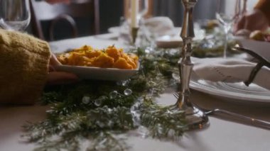 Tanınmayacak haldeki kadının elleri, kavrulmuş balkabağını Noel yemeği için çam dalları, kristal boncuklar ve mumlarla süslenmiş şenlik masasına yerleştirirken.