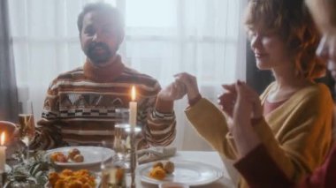 Aile üyeleri ev yapımı yemekler, mumlar ve yemyeşil çelenklerle dolu festival masalarında oturmuş, evde Noel yemeği yerken el ele tutuşup, gözleri kapalı dua ediyorlar.
