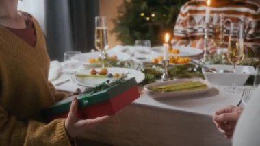 Evdeki Noel yemeği partisinde mum ışığında şenlik masasında birlikte otururken bir kadının kocasına Noel hediyesi vermesi yakın plan.