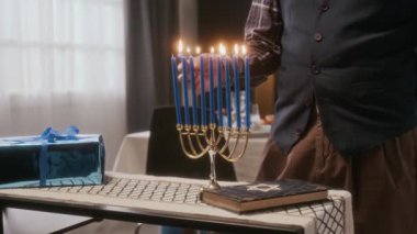 Evdeki Yahudi bayramı kutlaması için hazırlanırken yan masada hediye kutusu ve İbranice İncil 'le menorah mumları yakan tanınmamış adamı yakın çekim yapın.