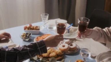 Hanukkah 'ı evde kutlarken bayramlık yemek masasında geleneksel Yahudi yemeği eşliğinde kadeh tokuşturup kadeh tokuşturan çiftlerin ellerine yakından bakın.