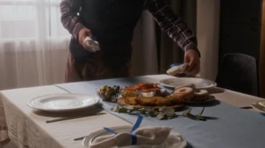 Evdeki Hanuka yemeğine hazırlanırken, geleneksel Yahudi yemekleriyle süslenmiş masalara mavi kurdelelerle süslenmiş beyaz peçeteler yerleştiren adamı yakından çek.