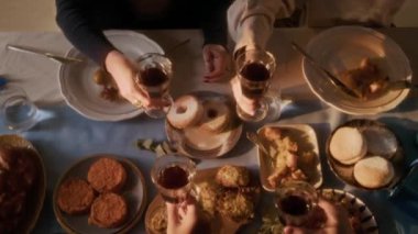 Yahudi aile üyelerinin Hanuka yemeği sırasında sıcak ışıklı şenlik masasında kırmızı Kiddush şarabıyla kadeh kaldırışlarını yukarıdan aşağı seyrediyorum.