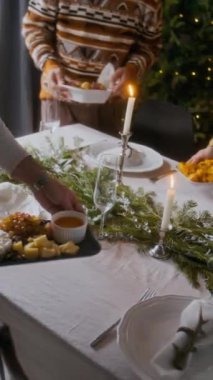 Noel yemeği için mum ışığı ve yemyeşil dallarla süslenmiş bayram masasında peynir tahtası ve şenlik yemekleriyle servis edilen aile fotoğrafı.