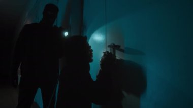 Afrika kökenli Amerikalı soyguncu gece kilidi açıyor, Kafkas suç ortağı kapıya fener tutuyor ve etrafa bakıyor.