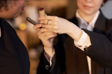 Tanınmayan bir kadın müşterinin, tanınmayan bir şarap şişesinin mantarını koklayan orta boy görüntüsü.