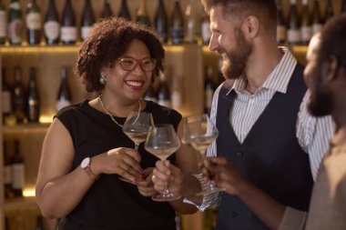 Karışık ırk güzel kadın gülümsüyor ve şarap mahzenindeki degulasyon sırasında meslektaşlarıyla beyaz şarap dolu kadehleri tokuşturuyor.