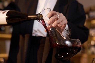 Çiçek açmak için cam sürahiye kırmızı şarap döken şarap garsonunun zarif, tanınmaz kadın eli orta boy.