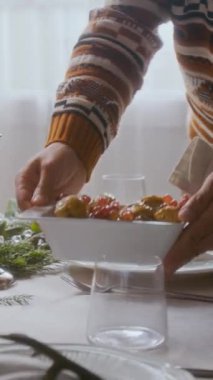 Evdeki Noel kutlaması için hazırlanırken, yemek masasında ev yapımı yemek servisi yapan tanınmayan bir adamın dikey yakın çekimi.