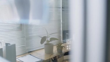Masasında saksı bitkileri, dokümanlar, sabit ekran ve göğüs röntgenini gösteren bilgisayar ekranı olan temiz ve düzenli tıbbi ofis çalışma alanının şeffaf ayırma duvarından bak