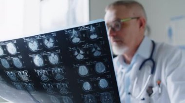 Klinikteki konsültasyon sırasında hastasıyla konuşurken MR taraması yapan orta yaşlı erkek doktorun yakın çekim görüntüleri.