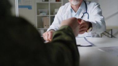 Tanımlanamayan asker termometreyi laboratuvar önlüklü orta yaşlı erkek doktora uzatıyor. Vücut ısısı hakkında yorum yapıyor ve kağıda yazıyor.