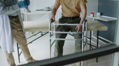 Çatışmada yaralanan askerin, yürüyen kareye yaslanıp, bacağındaki yarayı açıklarken, doktor klinikteki randevusu sırasında durumu hakkında sorular sorarken...