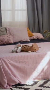 Pembe çarşaflı ve yastıklı, dikey yatak odası, gri perdeli, bitki, desenli siyah ve beyaz halı, kulaklık ve çanta.