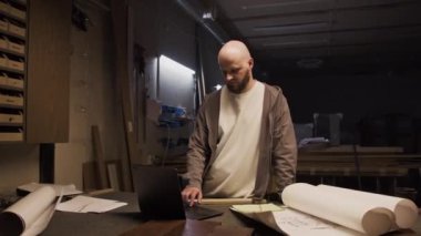 Profesyonel ahşap işçisinin dizüstü bilgisayarla portre fotoğrafını büyüt, sonra kollarını çapraz yap ve marangozluk atölyesinde kendine güvenle kameraya poz ver.