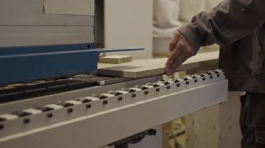 Erkek işçilerin, mobilya atölyesinde kenar şerit makinesinin taşıyıcı bandına ahşap panel yerleştirme görüntülerini kapat