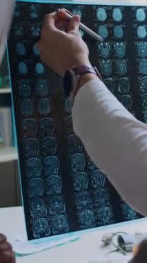 MRI 'ı tanımlayamayan doktorun dikey yakın çekimi, tarama yapmak ve hastasına kalemle önemli kısımlarını göstermek.