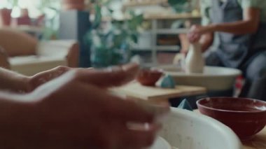 Kadın esnaf stüdyoda çömlekçi çarklarında vazo şekillendirirken, bilinmeyen bir zanaatkarın kilden kase oluşturmasına odaklan.