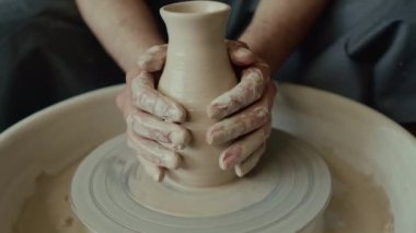Yakından bakınca, bilinmeyen bir erkek zanaatkarın çömlekçi çarkında şekillendirirken ellerini kilden vazonun üzerine koyduğunu görüyoruz.