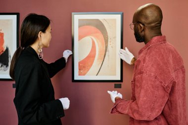 Galeri çalışanları karanlık ve gündelik giysiler içinde, galeride asılı duran modern soyut tabloyu tartışıyorlardı. Tarz ortamı sanatla bağın altını çizer