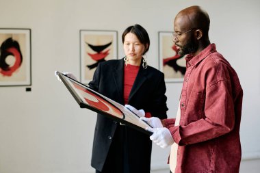 İki kişi, soyut resimlere odaklanmış bir galeri ortamında modern sanat eserlerini dikkatle inceliyor ve ilgi çekici bir tartışma sırasında ele geçiriliyor.