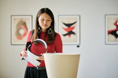 Heykeltıraş, iyi aydınlatılmış sanat galerisi ekipmanlarının içinde modern sanat eserleriyle meşgul. Arka plandaki duvarlarda gösterilen soyut sanat eserleri sanatsal ambiyansa katkıda bulunuyor