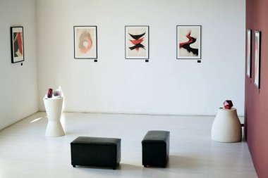 Etrafına siyah mobilyalar ve heykeller yerleştirilmiş beyaz duvarlarda soyut resimler sergilenen modern sanat galerisi. Geniş iç mekan sanat meraklıları için huzurlu bir deneyim sunuyor