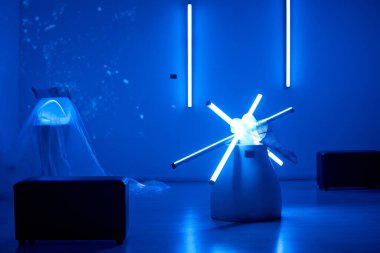 Minimalist sanat galerisini aydınlatan mavi ışıkla parıldayan neon kurulumunu tecrübe ediyorum. Sanatsal ambiyansı tamamlayan fütürist tasarımlar ve parlak ışık tüpleri