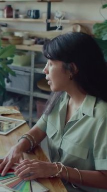 Esmer Latin kadın tasarımcının iş arkadaşlarıyla renk paletini tartışırken stüdyoda yeni bir proje üzerinde çalışırken dikey görünümü