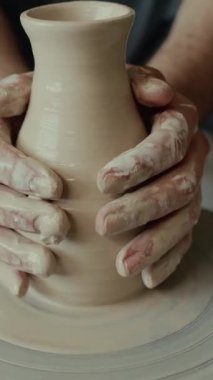 Tekerlek üzerinde kil vazo oluşturan tanınmayan çömlekçinin yumuşak ellerinden dikey yakın çekim.