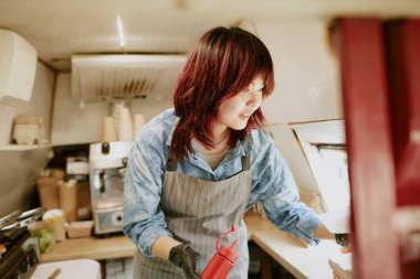 Ketçaplı Asyalı kadın aşçı elinde şişe sıkar yüzünde hafif bir gülümsemeyle sipariş verir.