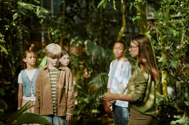 Genç bayan tur rehberi ve bir grup genç botanik bahçesindeki çeşitli yeşil bitkileri keşfediyorlar.