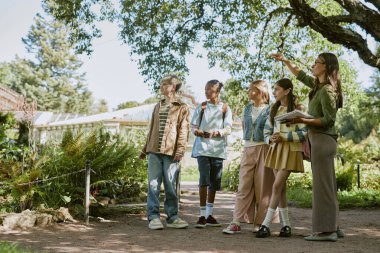 Genç bayan botanik çalışanı turne sırasında nadir bulunan bitkileri bir grup genç öğrenciye gösteriyor.