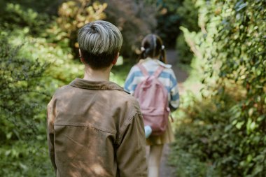 Güneşli bir sonbahar gününde botanik bahçesinde yürüyen tanınmayan genç kız ve oğlanın arka görüntüsü.