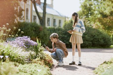 Kız dijital tablet üzerindeki verileri kontrol ederken, oğlanın parktaki bitkileri büyüteçle incelediği geniş açı, boşluk kopyala