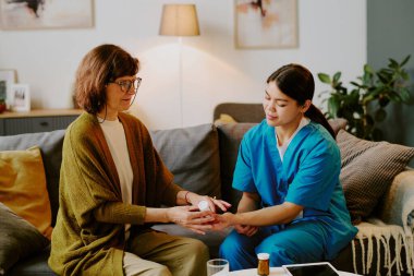 Hasta kanepede otururken, yaşlı bir kadına yardım eden hemşire oturma odası dekorunun sıcak ve davetkar olduğunu gösteriyor.