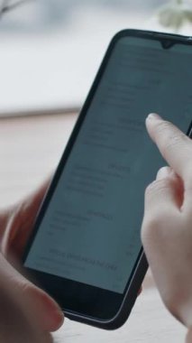 Kafede dijital menü okuyarak akıllı telefonuna odaklanan tanınmayan bir kadının omuz üstü fotoğrafı.
