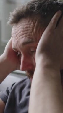 Bir adamın hayal kırıklığı içinde yüzünü ovalarken, terapi seansı boyunca endişeli olduğu dikey yakın çekim.