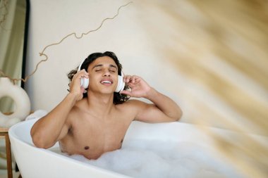 Gözleri kapalı melez bir adam ve kulaklıkla müzik dinlerken sıcak bir banyo yapan bir gülümseme.